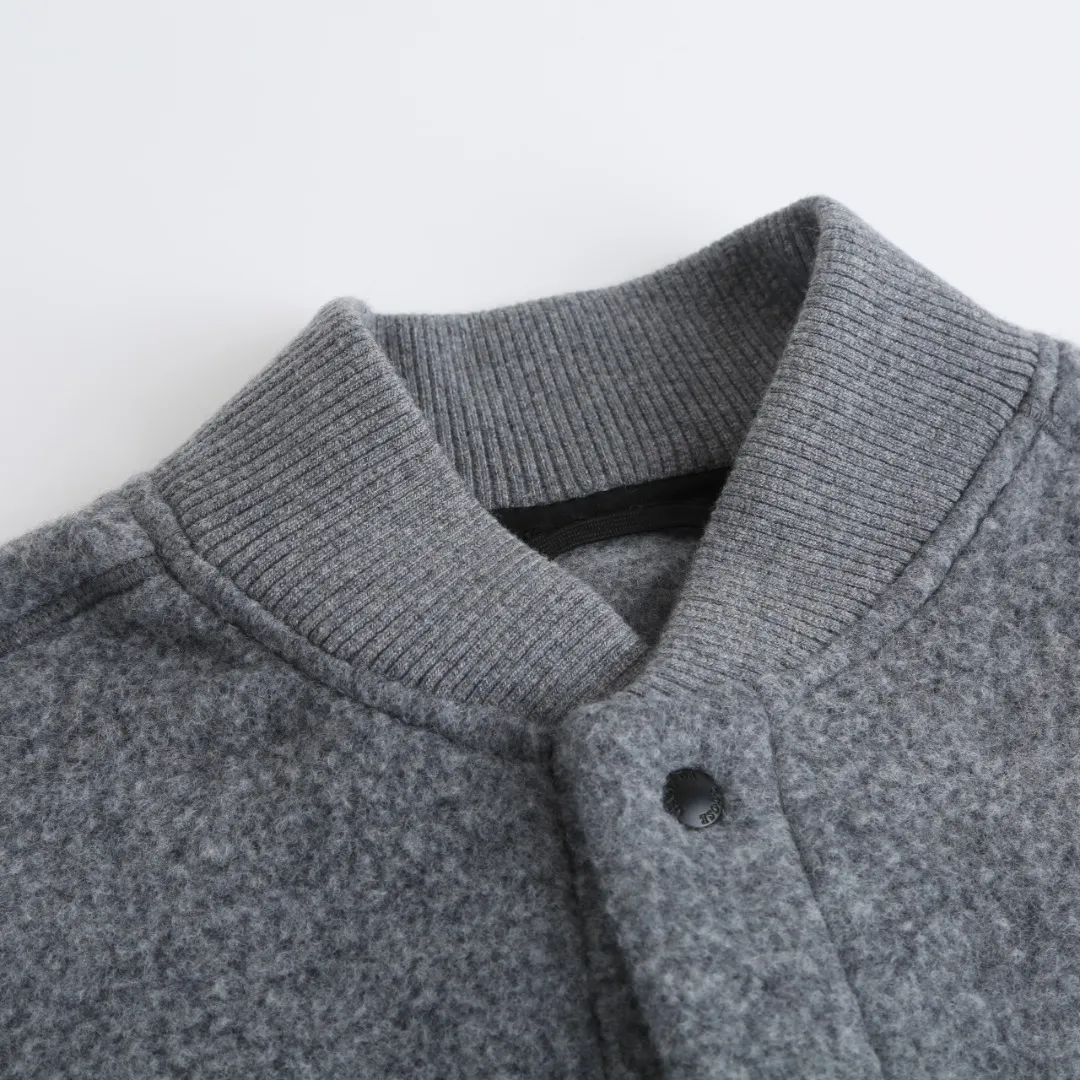 P760 Canada Goose Fleece Badge Button Jacket Fabric selection: Wool blend fabric: The main fabric of this jacket is light gray wool blend fabric to improve the fabric's wear resistance, wrinkle resistance and warmth. Wool provides good warmth and a natural feel, while blended fibers enhance the fabric's practicality and durability.  RIBBED KNIT: The collar, cuffs and hem are ribbed knitted for added stretch and fit.  Production process: The cutting process needs to ensure that the texture and color of the fabric are evenly distributed, especially for this light gray tone, to avoid color differences. The stretchability of wool-blend fabrics needs to be taken into consideration when cutting pieces to ensure dimensional stability of the finished garment.      • Use a sewing needle and thread suitable for wool-blend fabrics to avoid damage to the fabric during sewing. The sewing stitches are even and firm to prevent thread stripping.      • The temperature needs to be controlled during ironing to avoid high temperature damage to the fabric while keeping the fabric smooth and crisp.  Main body splicing: • The front and back body parts, sleeves and other main parts are spliced ​​with flat seams to ensure a smooth silhouette. •Align the fabric texture at the splicing points to keep the appearance neat.     Details such as pockets and cuffs are designed with inset pockets to increase practicality and aesthetics.     The splicing areas are reinforced to improve durability.  Armband: The white round armband on the left arm is an important part of the brand identity and is finely sewn to ensure it is strong and flat.  Dark gray and light gray Size: S M L XL